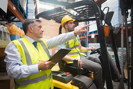 Forklift driver talking with his manager in a large warehouseの写真素材
