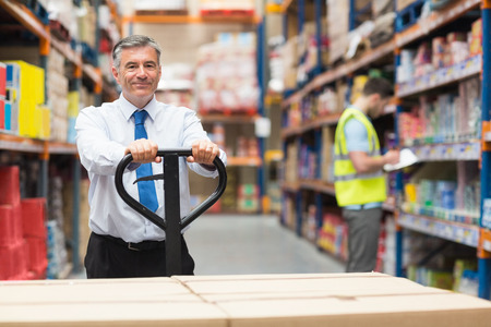 Manager pulling trolley with boxes in front of his employee in warehouseの写真素材