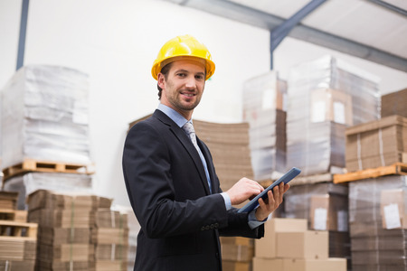 Warehouse manager wearing hard hat using tablet in a large warehouseの写真素材