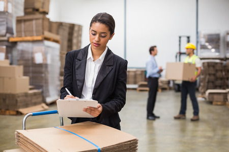 Pretty warehouse manager writing on clipboard in a large warehouseの写真素材