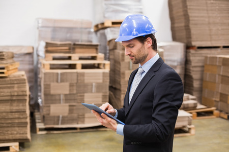 Warehouse manager wearing hard hat using tablet in a large warehouseの写真素材