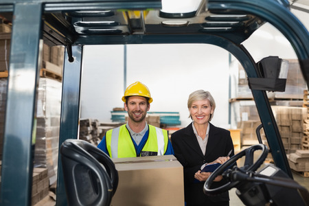 Warehouse manager smiling at camera with forklift driver in a large warehouseの写真素材