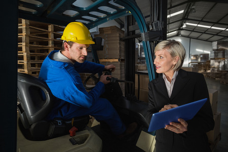 Forklift driver talking with his manager in a large warehouseの写真素材