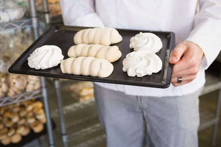 Mid section of baker holding meringue tray at the bakeryの写真素材