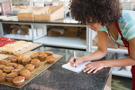Pretty waitress writing on notebook at the bakeryの写真素材