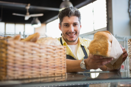 Cheerful worker standing and presenting a bread at the bakery