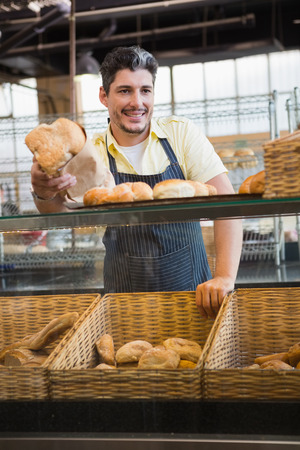 Portrait of smiling server offering bread at the bakeryの写真素材