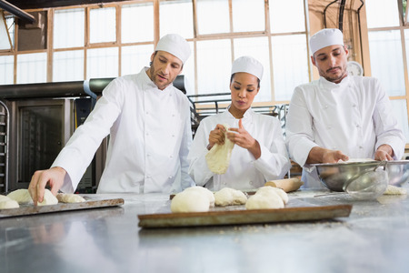 Concentrated colleagues kneading uncooked dough in the kitchen of the bakeryの写真素材