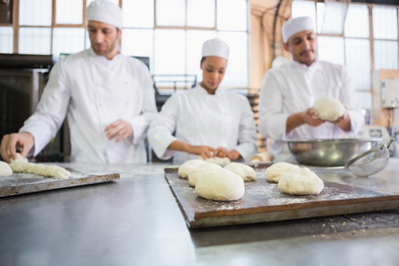 Serious colleagues kneading uncooked dough in the kitchen of the bakeryの写真素材