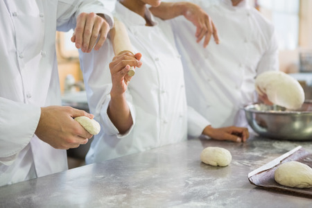 Colleagues holding rolling pin and dough in the kitchen of the bakeryの写真素材