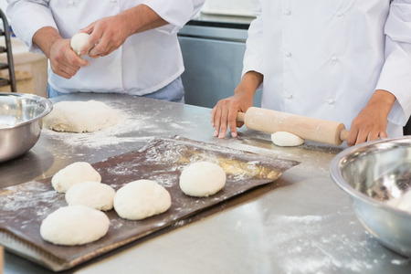 Co-workers kneading uncooked dough together in the kitchen of the bakery