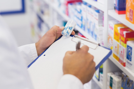 Pharmacist writing on clipboard and holding medicine jar at the hospital pharmacyの写真素材
