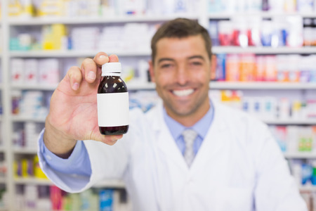 Handsome pharmacist showing medicine bottle at the hospital pharmacyの写真素材