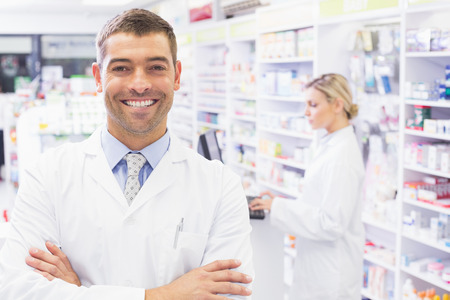 Smiling tpharmacist standing with arms crossed in the pharmacyの写真素材