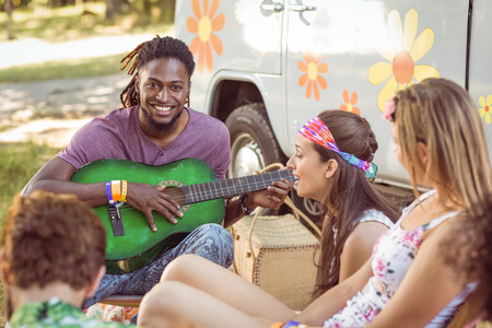 Happy hipster smiling at camera playing guitar at a music festivalの写真素材