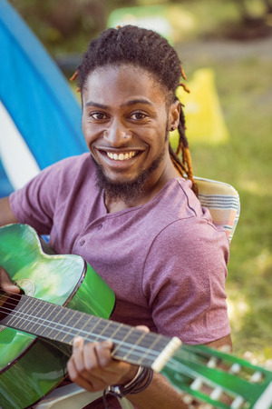 Happy hipster smiling at camera playing guitar at a music festivalの写真素材