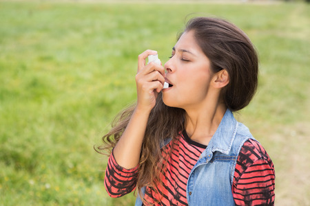 Pretty brunette using her inhaler on a sunny dayの写真素材