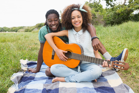 Young couple on a picnic playing guitar on a sunny day