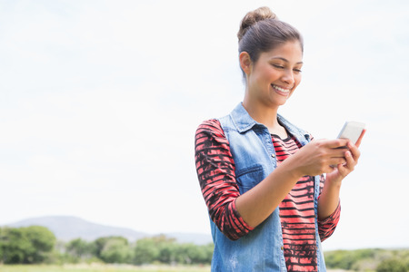 Pretty brunette texting in the park on a sunny dayの写真素材