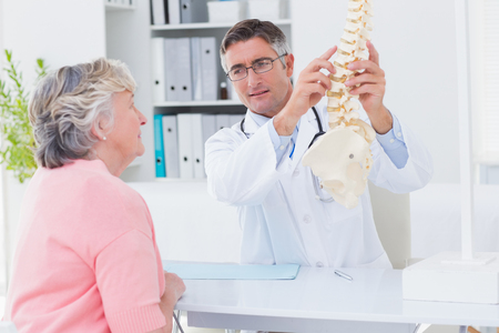Male doctor explaning anatomical spine to female patient in clinicの写真素材