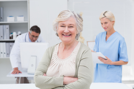 Portrait of senior patient smiling while doctor and nurse working in background at clinicの写真素材