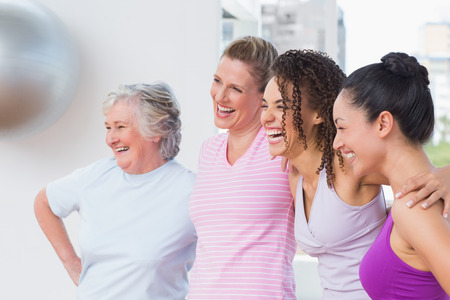 Happy female friends standing arms around in fitness studioの写真素材