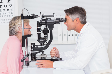 Side view of optician examining senior patient through slit lamp in clinicの写真素材