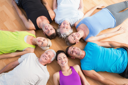 High angle view of happy people lying in circle on hardwood floor at gymの写真素材