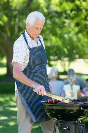 Concentrate grandfather doing barbecue on a sunny dayの写真素材