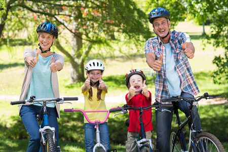 Happy family on their bike with thumbs up at the park on a sunny dayの写真素材