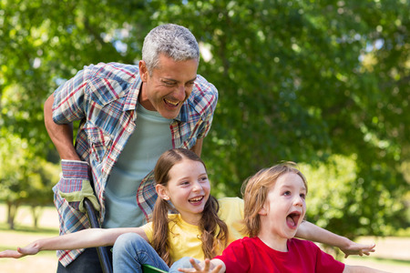 Happy father and his children playing with a wheelbarrow on a sunny day