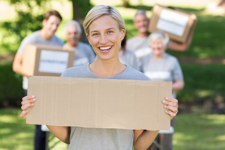 Happy volunteer blonde holding blank on a sunny day