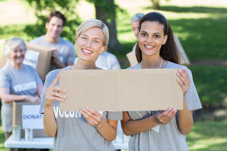 Happy volunteer friends holding blank on a sunny dayの写真素材