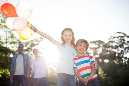 Happy siblings holding balloons at the park on a sunny dayの写真素材