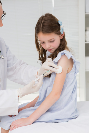 Doctor doing injection at a little girl in medical officeの写真素材