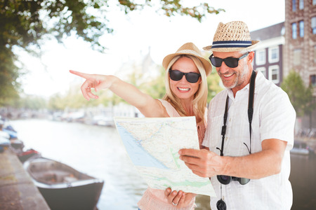 Happy tourist couple using map and pointing against canal in amsterdam
