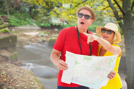 Happy tourist couple using map against rapids flowing along forest