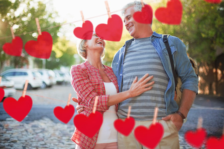 Happy mature couple hugging in the city against hearts hanging on a line