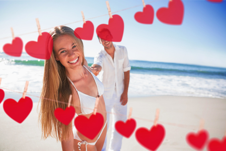 Woman smiling at camera with boyfriend holding her hand against hearts hanging on a lineの写真素材