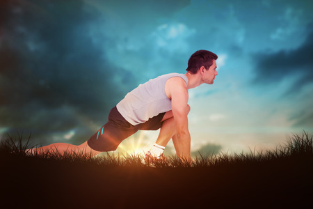 Side view of a young man in ready to run posture against blue sky over grass