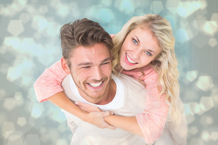 Handsome man giving piggy back to his girlfriend against light glowing dots design patternの写真素材