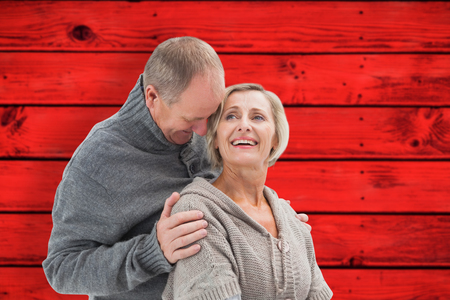 Happy mature couple in winter clothes against red wooden planksの写真素材