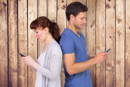 Couple both sending text messages against wooden planksの写真素材