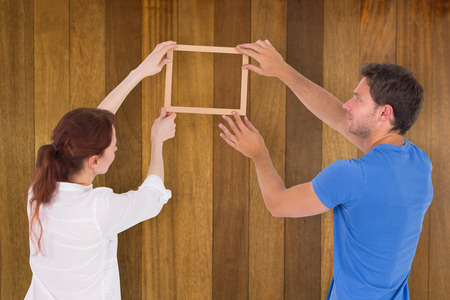 Couple deciding to hang picture against wooden surface with planksの写真素材