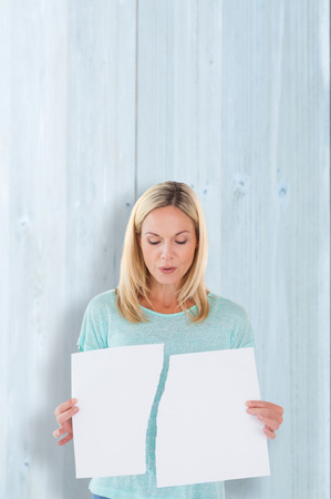 Serious woman holding torn sheet of paper against bleached wooden planks backgroundの写真素材