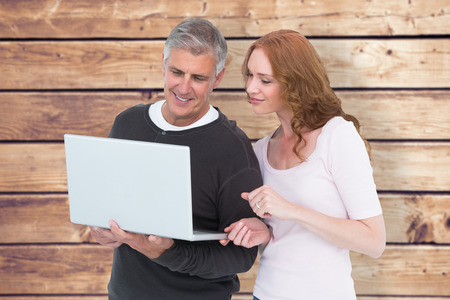 Casual couple using laptop together against wooden planks backgroundの写真素材