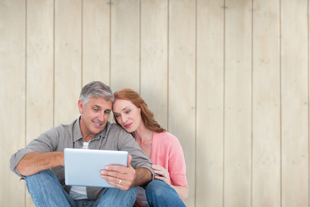 Casual couple sitting using tablet against wooden planksの写真素材