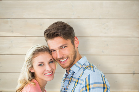Attractive couple smiling at camera against bleached wooden planks backgroundの写真素材