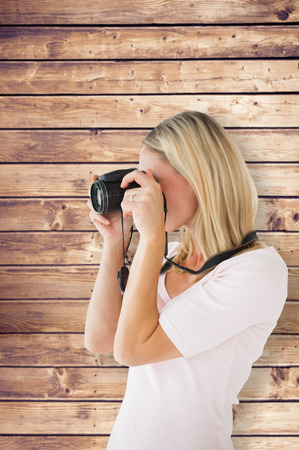 Happy blonde taking a photo on camera against wooden planksの写真素材
