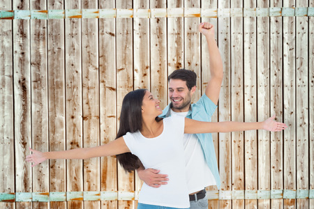 Happy casual couple cheering together against wooden background in pale woodの写真素材